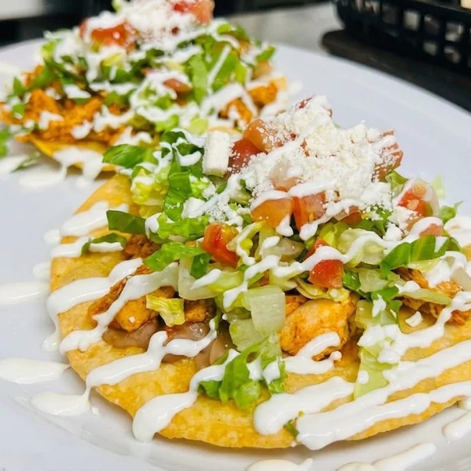 Two plates of loaded nachos topped with chicken, lettuce, tomatoes, cheese, and drizzled cream sauce.