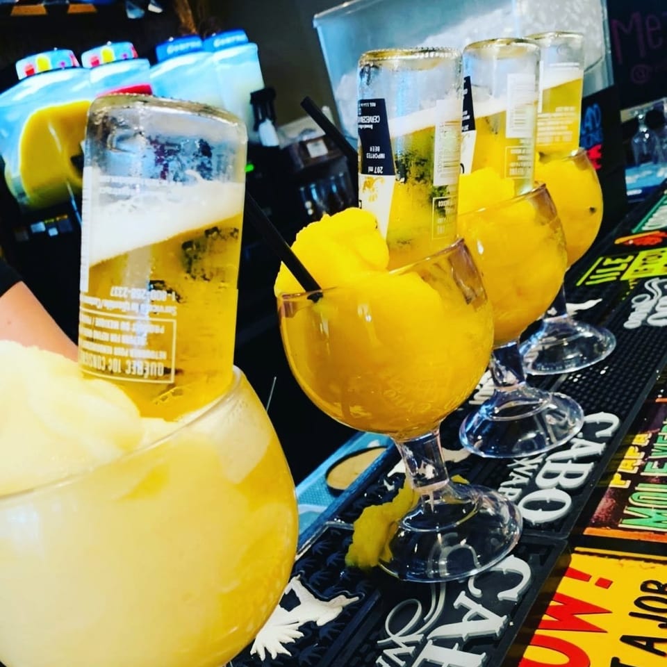 Yellow beer-filled goblets and oversized citrus cocktails sit on a colorful bar counter.