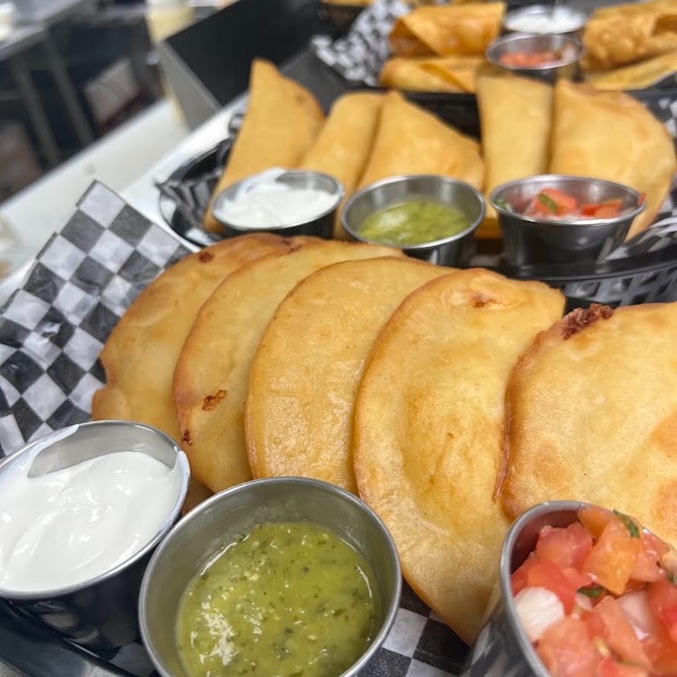 Golden stuffed pastries arranged in baskets with cups of creamy white sauce, green salsa, and pico de gallo.