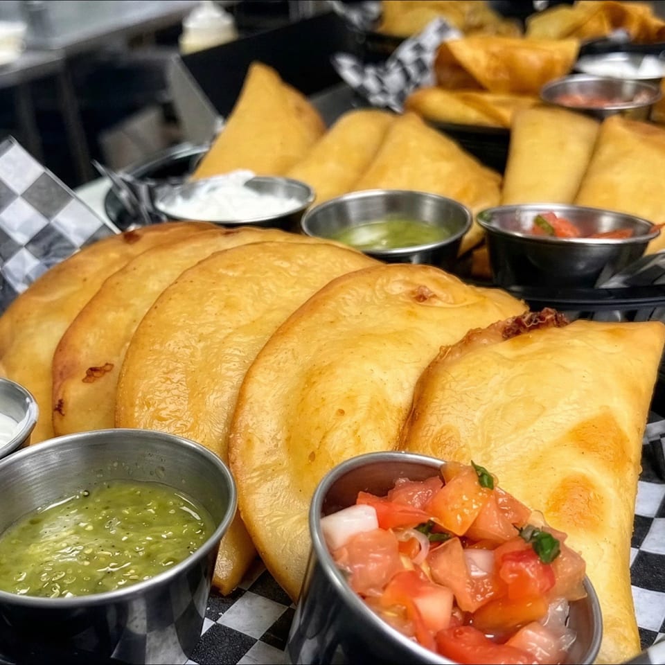 Golden fried empanadas served in checkered baskets with sour cream, green salsa, and pico de gallo.