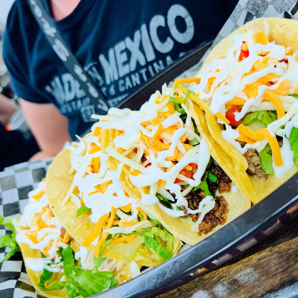 Loaded crunchy tacos topped with seasoned meat, lettuce, tomatoes, shredded cheese, and white sauce on a tray.