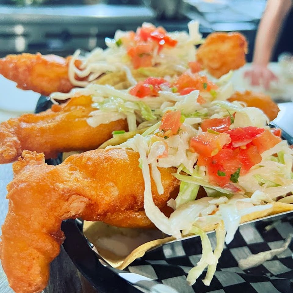 Crispy golden fish fillets topped with shredded lettuce and diced tomatoes on a checkered serving basket.